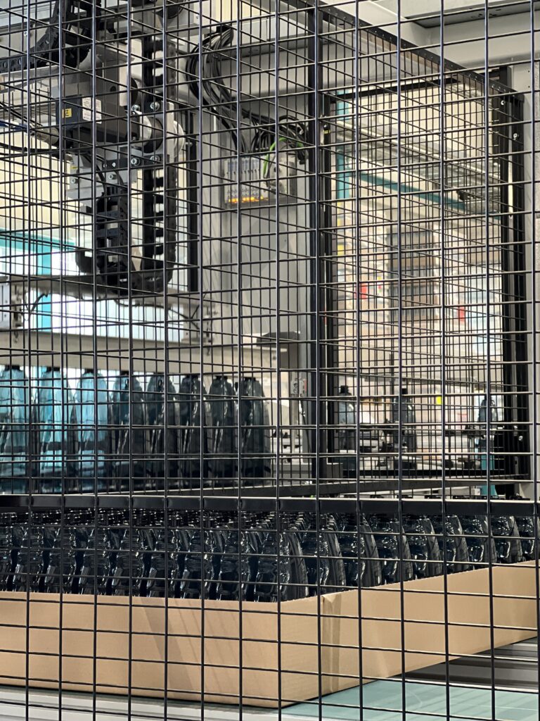 Schwarze PET-Sprühflaschen der EPROPLAST GmbH stehen hinter Gittern in einer vollautomatisierten Verpackungsmaschine.